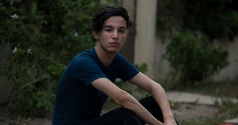 A teenage boy sitting on the curb