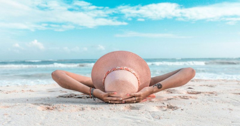 A woman in a hat laying on the beach while on vacation from her job, which gives her unlimited paid-time-off