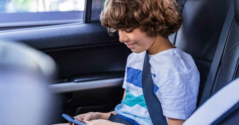 Teenage boy riding in the car with his aunt and playing on his phone